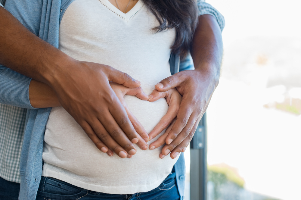 pregnant woman and man holding hands in heart shape on baby bump