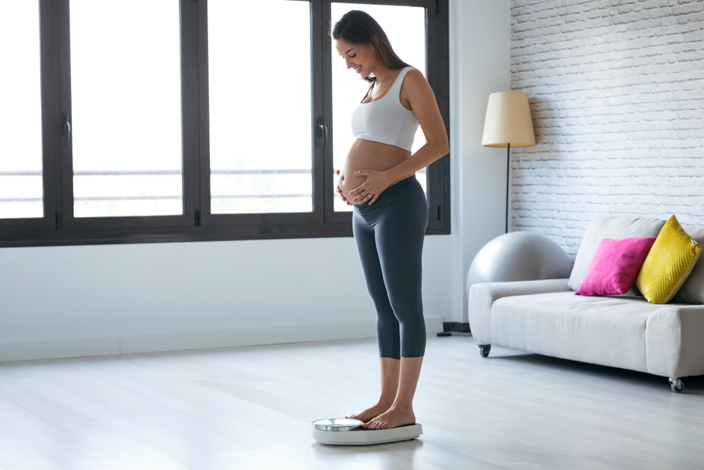 Pregnant woman stepping on scale.