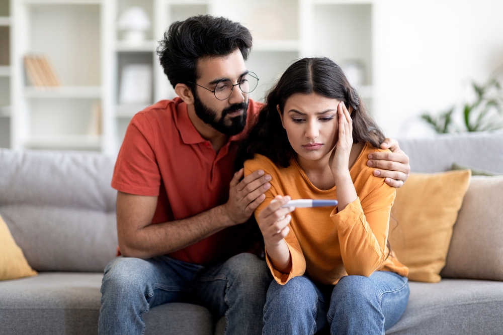 woman and man holding a pregnancy test, looking upset.
